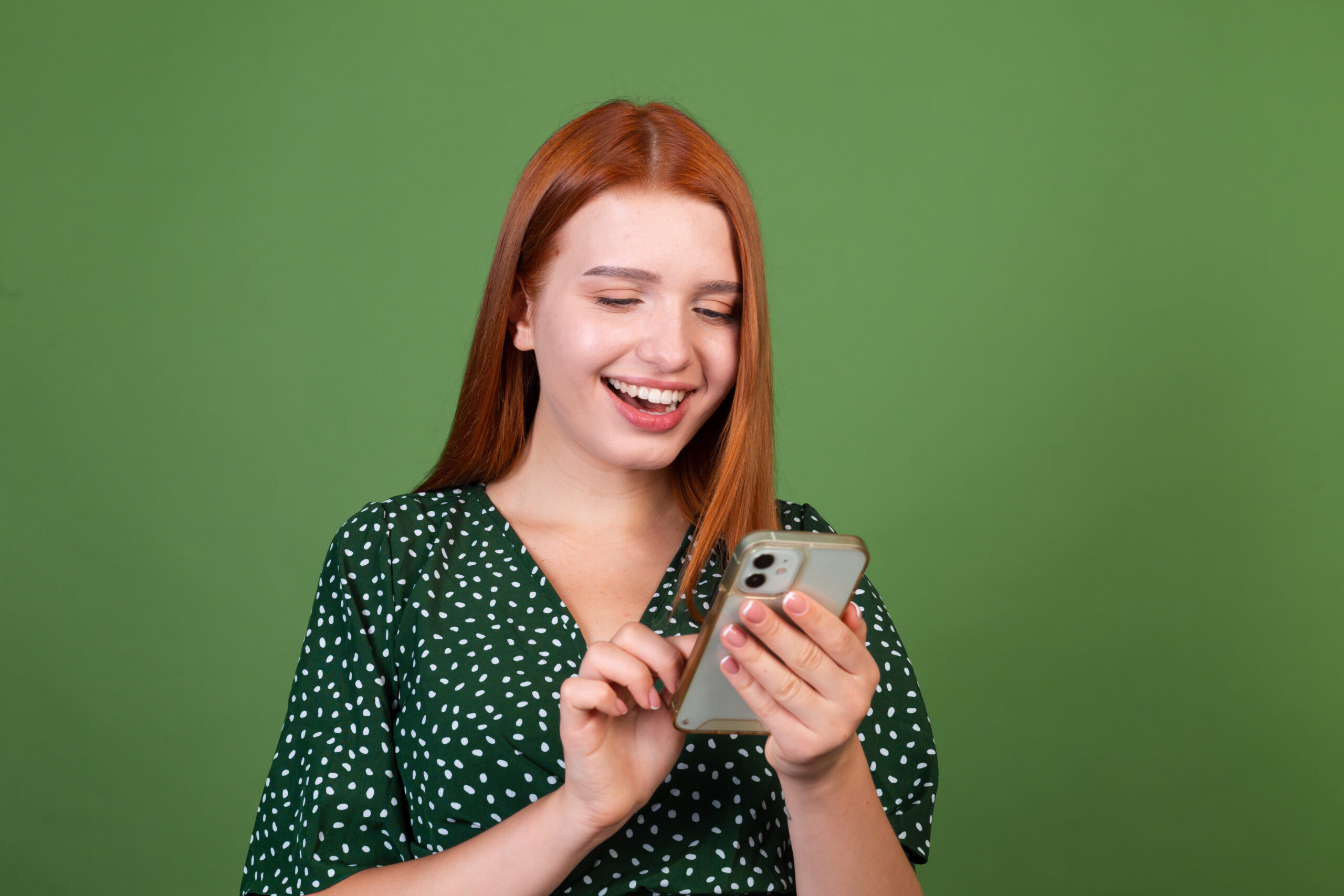 Young red hair woman on green background with  mobile phone happy positive excited
